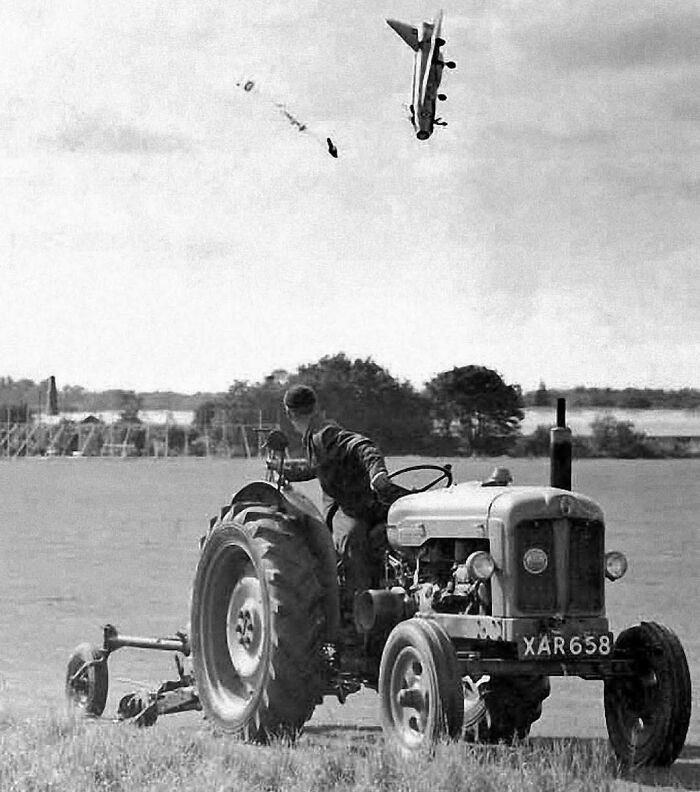 Vintage black and white photo of a farmer on a tractor witnessing a historic airplane crash.