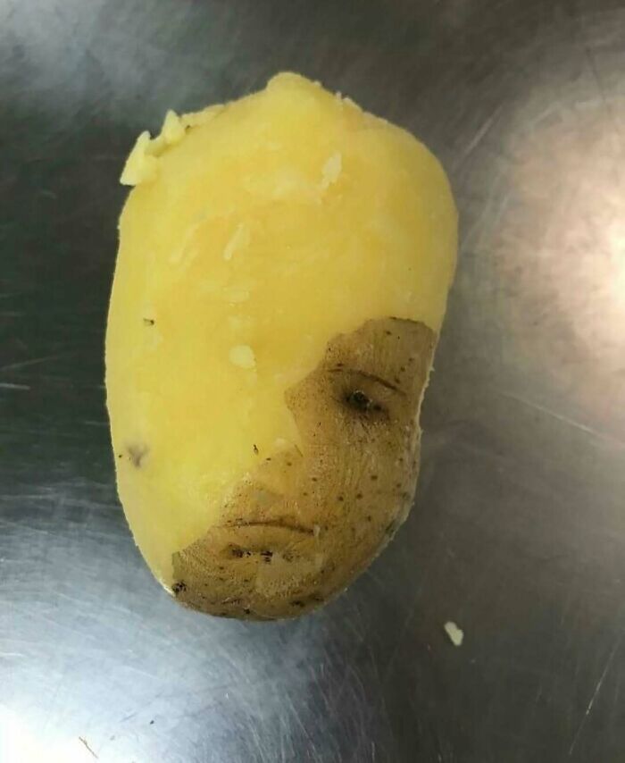 Partially peeled potato with a human face-like pattern on its skin, showcasing a bizarre nature and animal-related phenomenon.