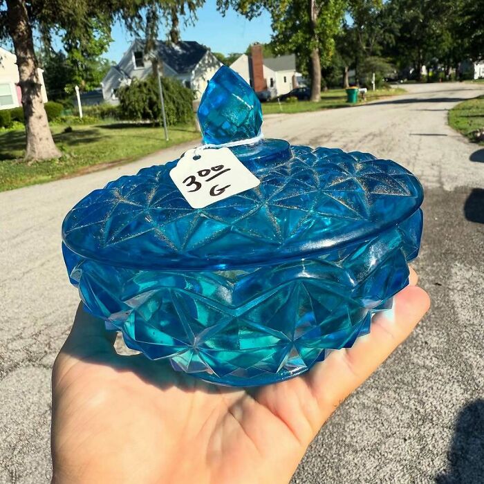 Hand holding a blue vintage glass container with lid, showcasing one of the best cool secondhand finds outdoors.