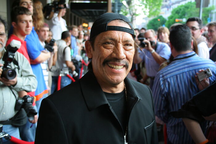 Smiling man wearing a backward cap at a crowded event, symbolizing late bloomers who became millionaires against odds.