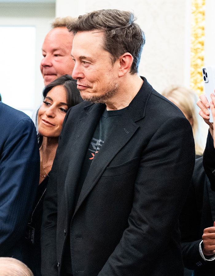 Elon Musk wearing a black blazer in a crowd, showing signs of sudden aging after feud with Donald Trump.