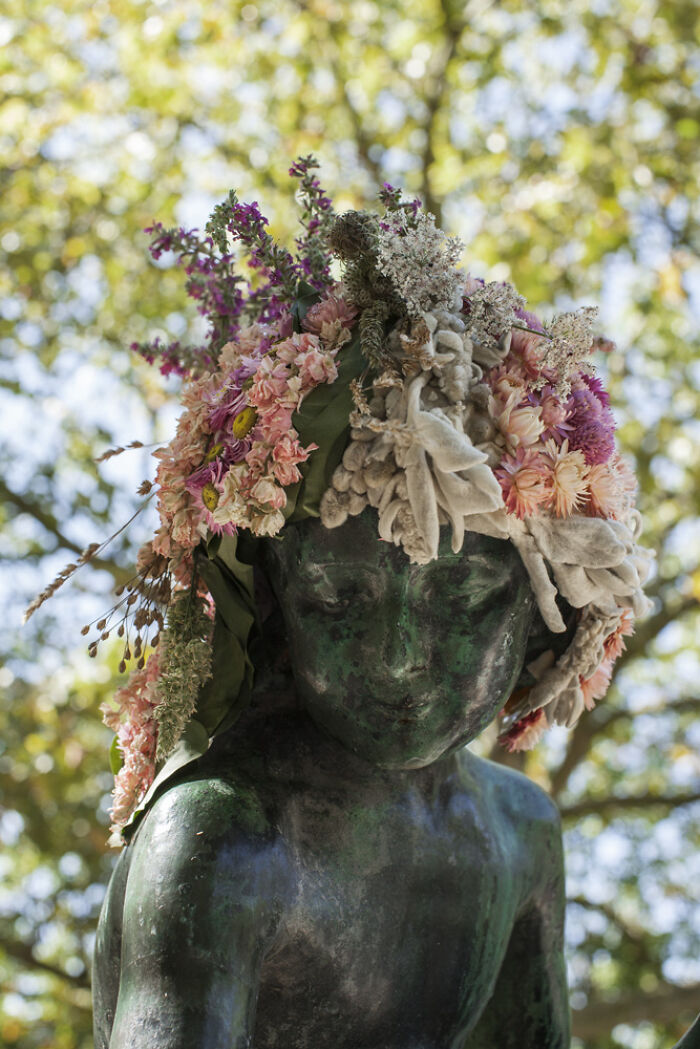 City statue adorned with a colorful floral crown created by an artist dressing city statues in flowers outdoors.