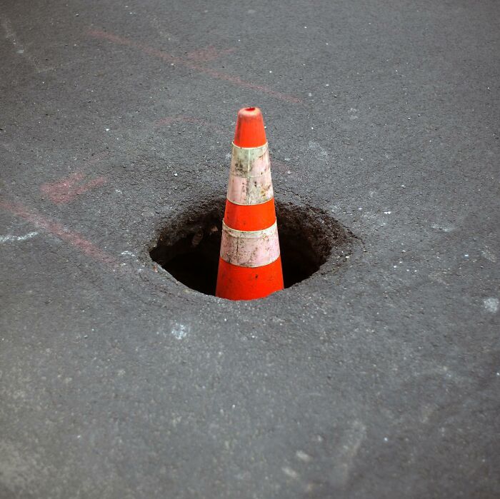 Orange traffic cone placed inside a hole on the street, capturing a street photographer's magical city life coincidence.