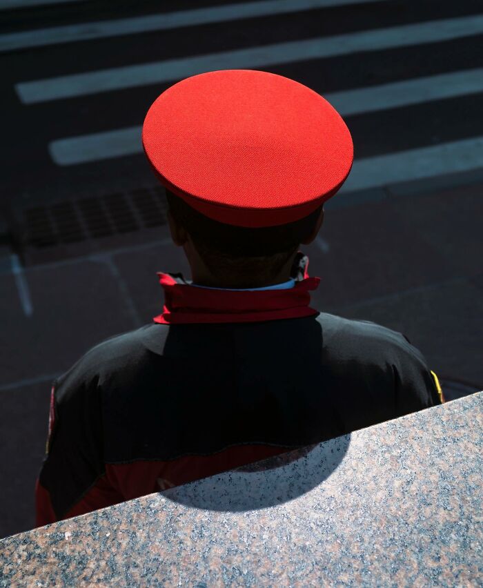 Man in red hat and uniform standing by a crosswalk, capturing street photographer’s magical city life coincidences.
