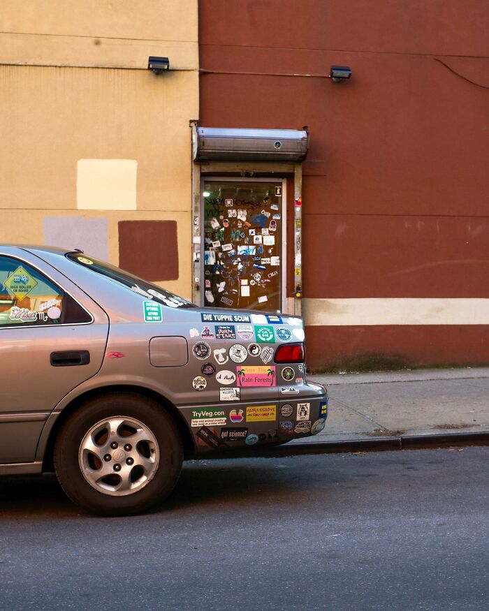 A street photographer captures a car covered in stickers parked by a graffiti-covered door in the city.