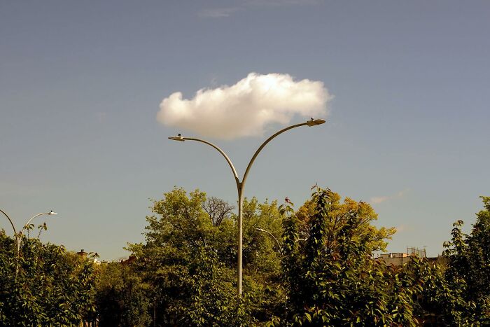 Street photographer captures magical city life coincidence with a cloud perfectly aligned above street lamps and trees.