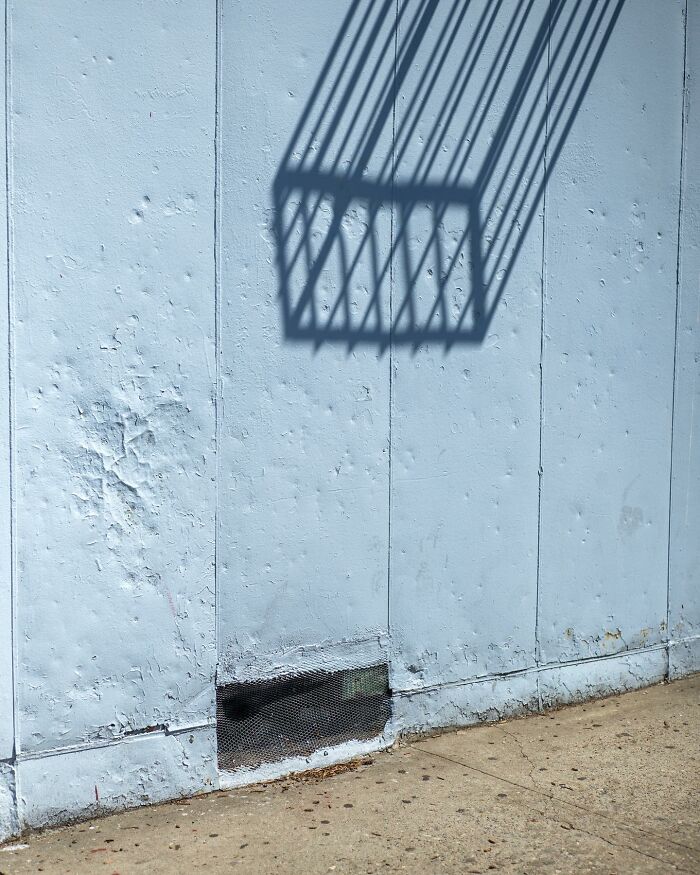 Shadow of a city fence casting a geometric pattern on a weathered blue wall in a street photographer’s magical city scene.