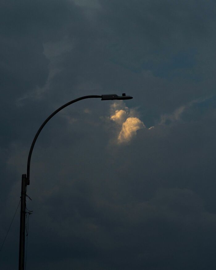 Street photographer captures magical city life with a glowing streetlamp against a dark cloudy sky at dusk.