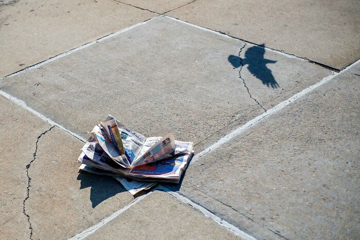 Shadow of flying bird perfectly aligned with crumpled newspaper on city sidewalk in a magical street photography moment.