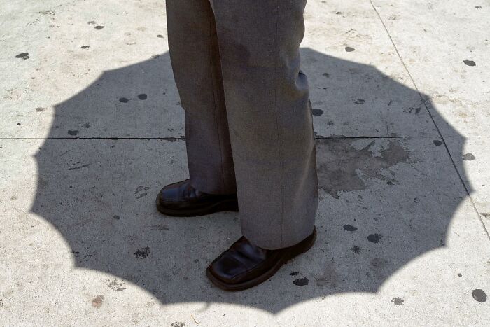 Shadow of an umbrella forming a perfect circle around a person’s feet on a city sidewalk street photography coincidence.