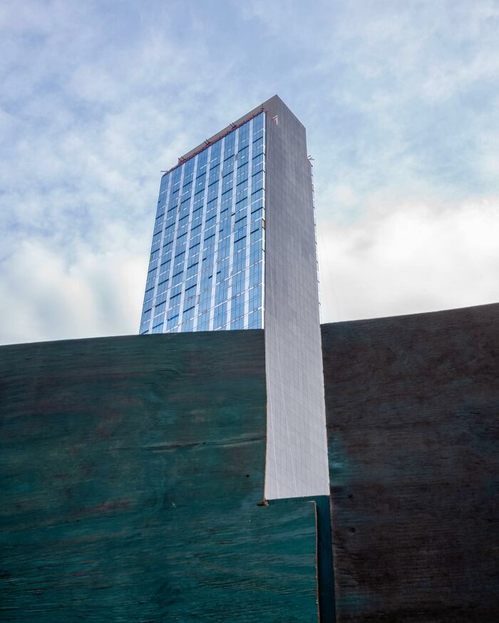 Modern glass building seen through a gap in large wooden panels, showcasing a magical street photography coincidence in the city.