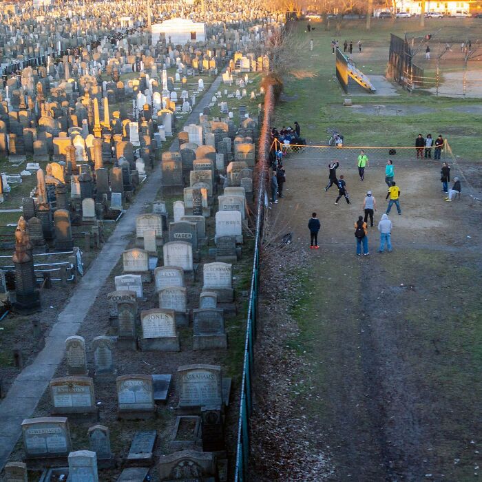 A street photographer captures a city scene with people playing volleyball beside a cemetery, showcasing magical coincidences.