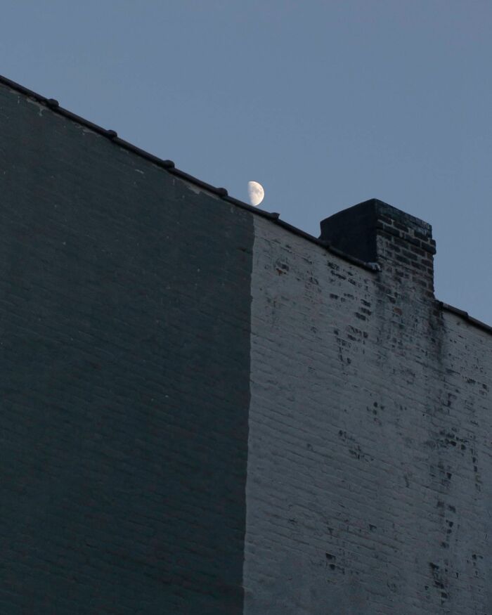 Half moon rising above a city building roof captured by street photographer highlighting magical city life coincidences.