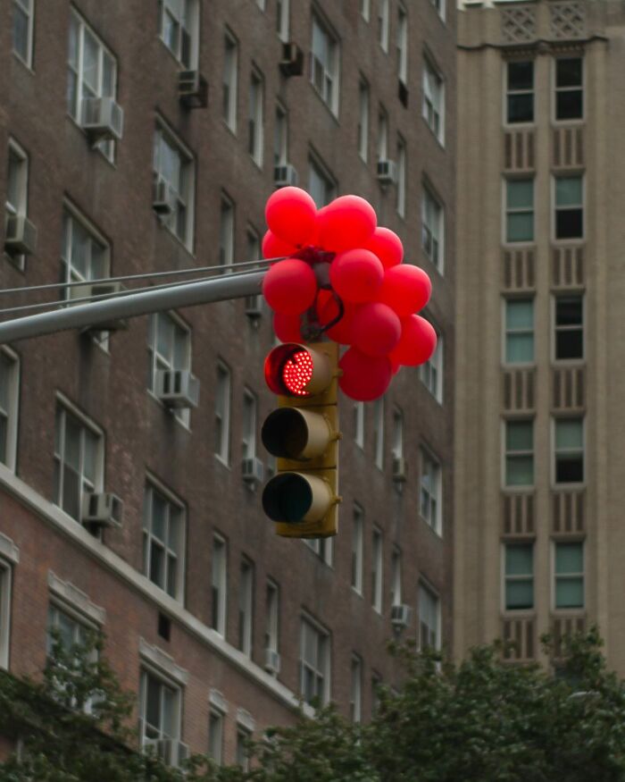 Red balloons cluster around a city traffic light showing red, capturing street photographer’s magical city life coincidence.