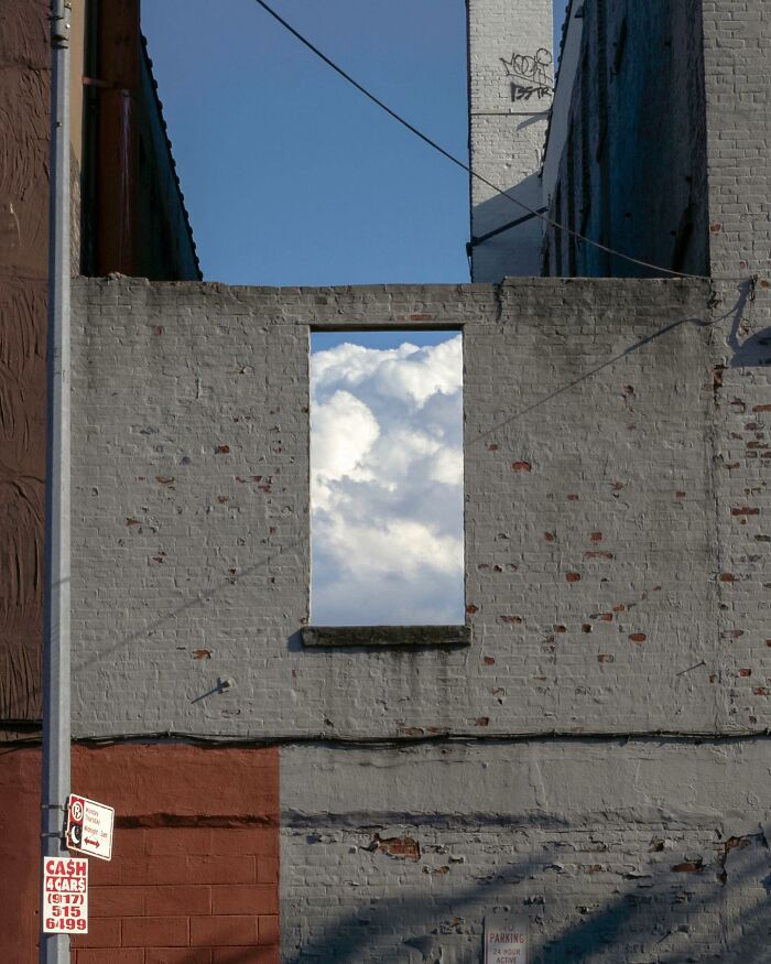 Urban street photography capturing a magical city moment with clouds perfectly framed through a window opening in a brick wall.