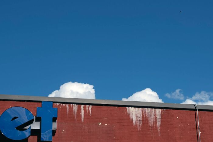 Partial blue sign on red brick wall with white stains against blue sky and clouds, showcasing magical city life coincidences.