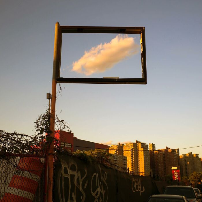 Street photographer captures city life coincidence of a cloud perfectly framed in an empty sign against urban buildings at sunset.