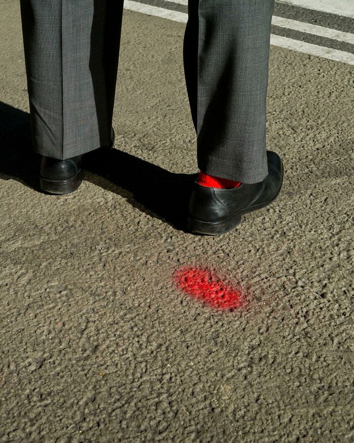Street photographer captures coincidence of matching red socks and red paint on urban street pavement.