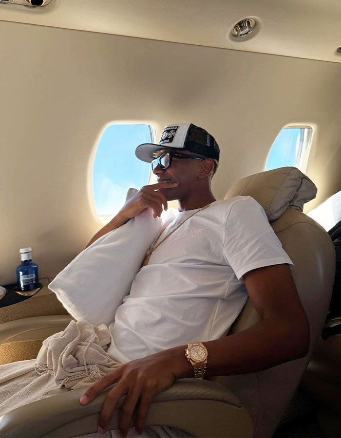 Influencer relaxing on private jet wearing sunglasses and hat, vacationing amid backlash and minor public controversy.