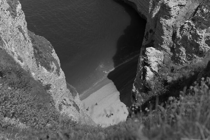 Black and white cinematic photo capturing a quiet beach between tall cliffs, showcasing everyday life details from above.