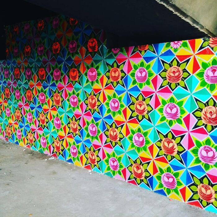Colorful intricate patterned mural covering a wall with vibrant geometric shapes and floral designs by an artist.