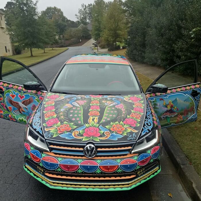 Volkswagen car decorated with colorful, intricate patterns featuring flowers, birds, and vibrant artistic designs.