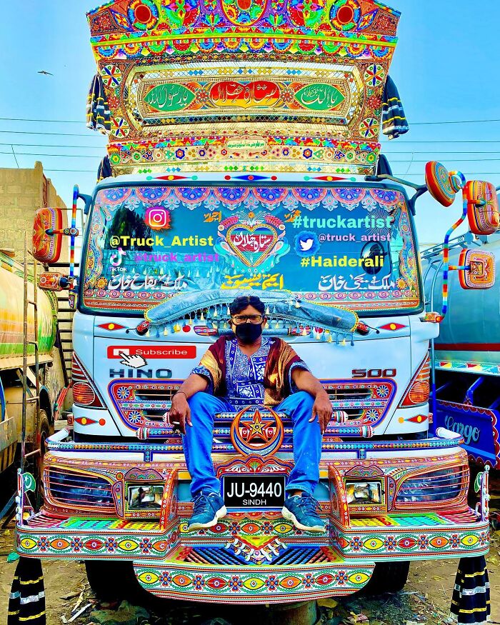 Man wearing mask sitting on a colorful truck covered in intricate patterns by a truck artist in Sindh.