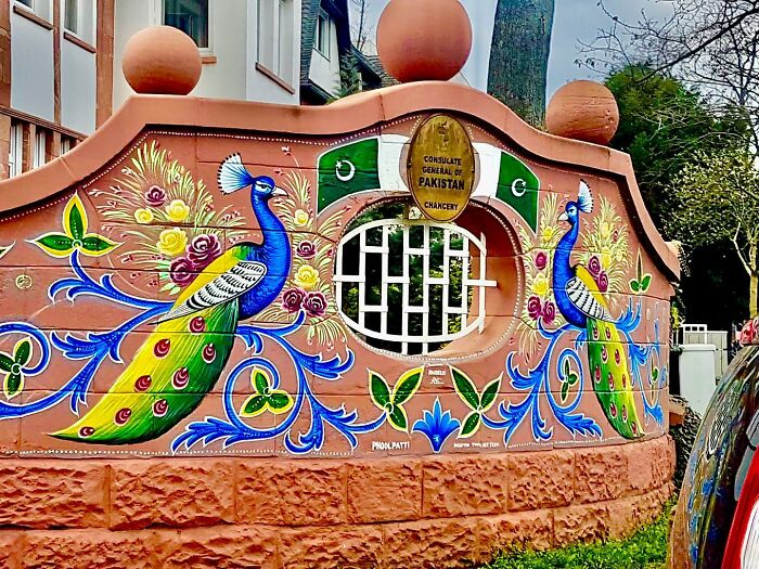 Intricate colorful patterns of peacocks and flowers painted on a wall, showcasing stunning works of art by an artist.