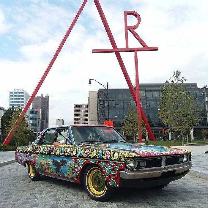 Colorful car artwork featuring intricate patterns and detailed designs displayed in an urban outdoor setting.