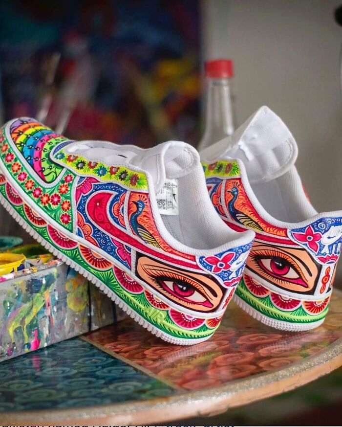 White sneakers painted with colorful, intricate patterns featuring eyes and floral designs by an artist transforming shoes into art.