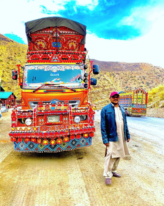 Man standing beside a colorful, intricately patterned truck, showcasing stunning works of art on vehicles outdoors.