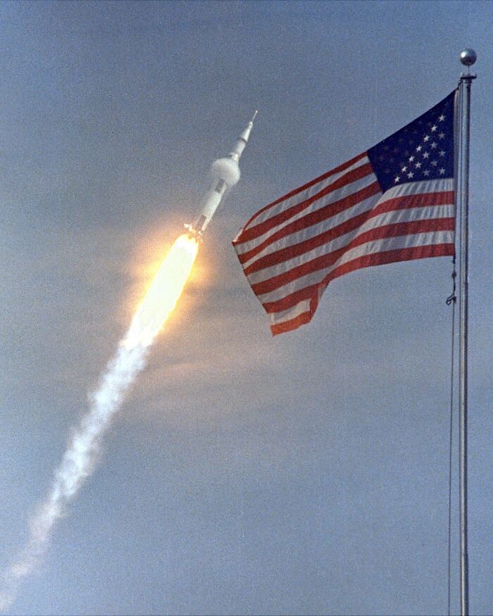 Apollo mission rocket launching with American flag flying against a clear sky during historic space exploration.