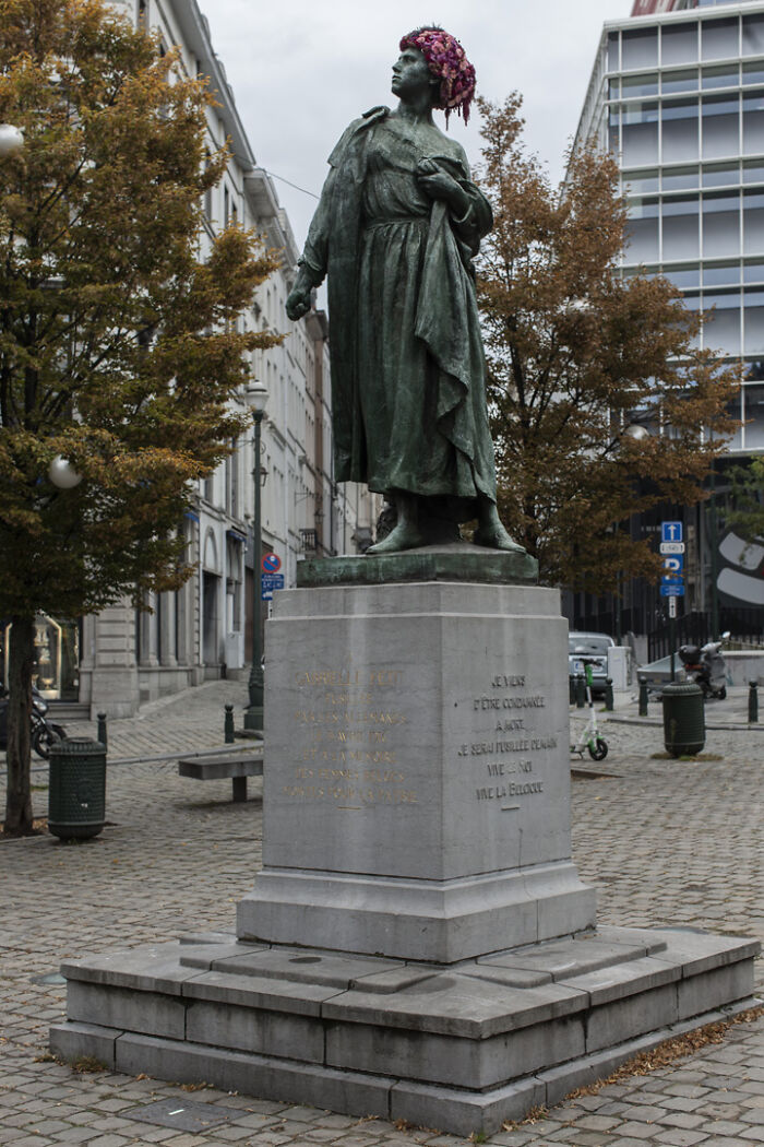Bronze city statue adorned with vibrant flowers on its head, showcasing artistic floral dressing in an urban setting.