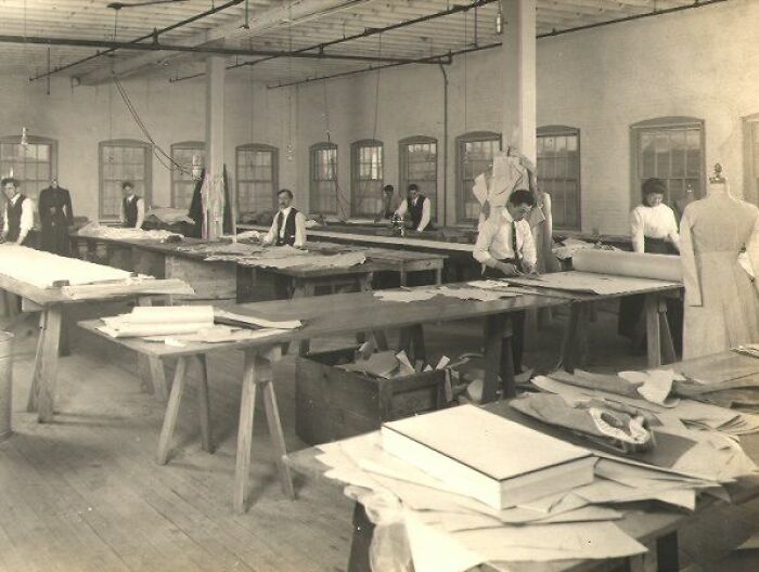 Vintage photo of American working class people in a garment factory measuring and cutting fabric for clothing production.
