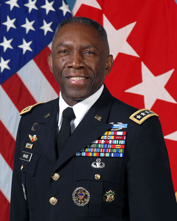 African American military leader in uniform with medals, standing in front of American and command flags.