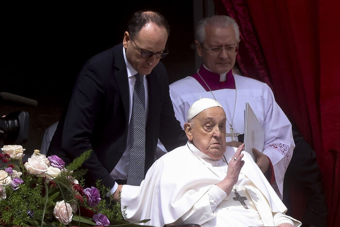 Pope Francis in one of the last known photos of famous people, seated and giving a blessing with attendants behind him.
