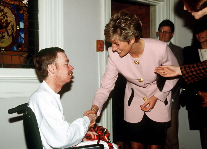 Princess Diana warmly shaking hands with a man in a wheelchair during a royal charitable event.