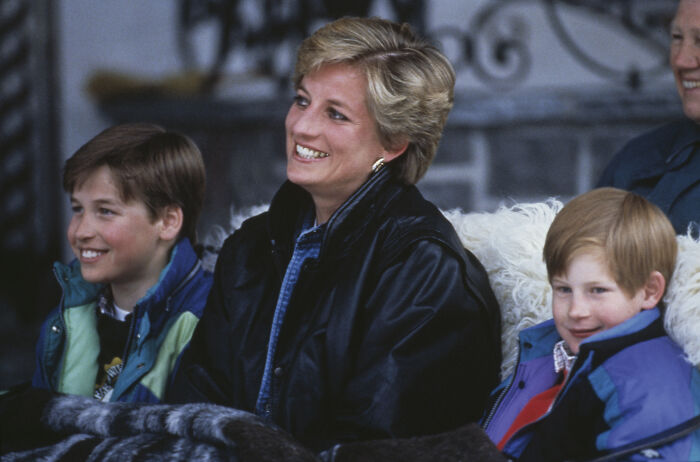 Princess Diana smiling warmly outdoors with her two sons dressed in colorful winter jackets.