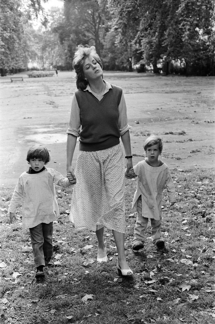 Princess Diana walking hand in hand with two young boys in a park, showcasing a rare candid family moment.