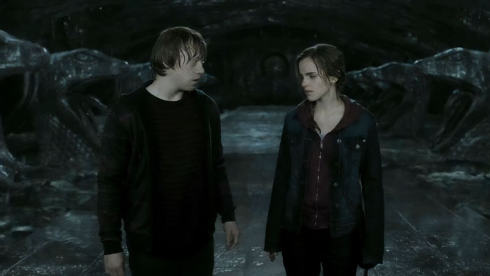 Emma Watson and Rupert Grint in a dark, cave-like setting from a Harry Potter film scene.