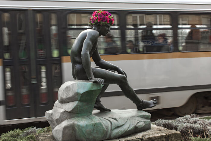 City statue wearing a vibrant floral crown, showcasing an artistic flower dress installation in an urban setting.