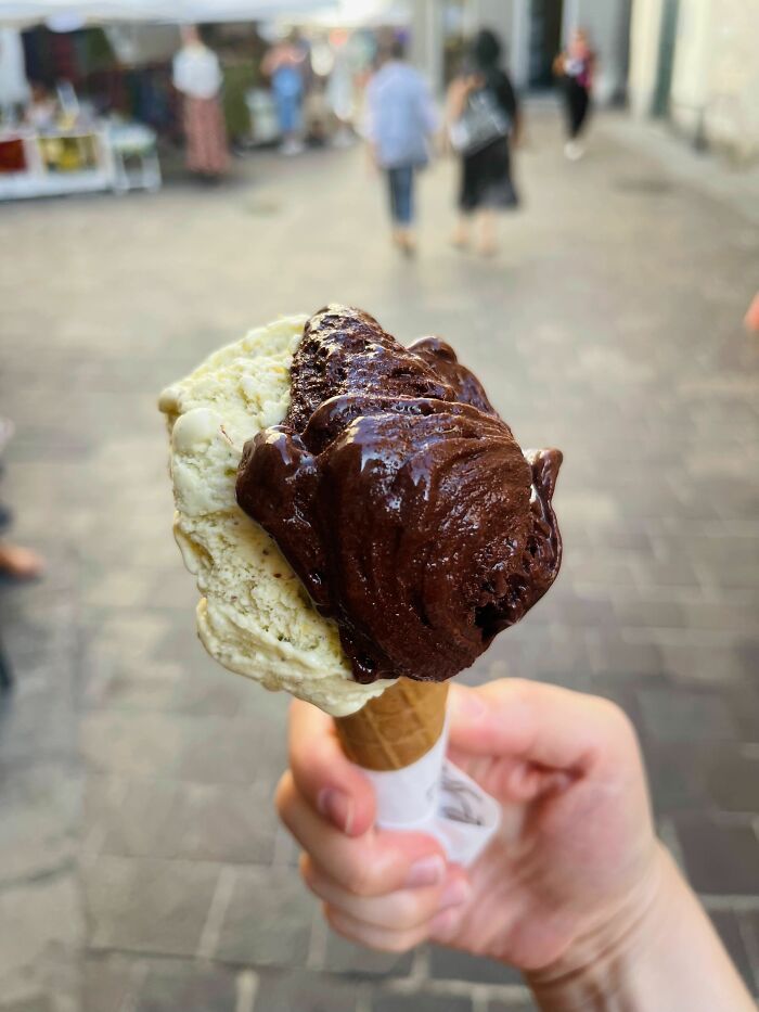 Hand holding a melting chocolate and vanilla ice cream cone, a perfect summer moment captured outdoors.