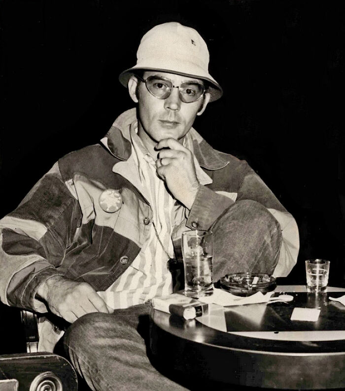 Man wearing glasses and a bucket hat sitting at a table, representing famous names from history good looking.