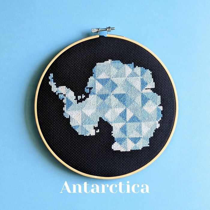 Cross-stitched map of Antarctica in blue and white thread on black fabric framed in embroidery hoop.