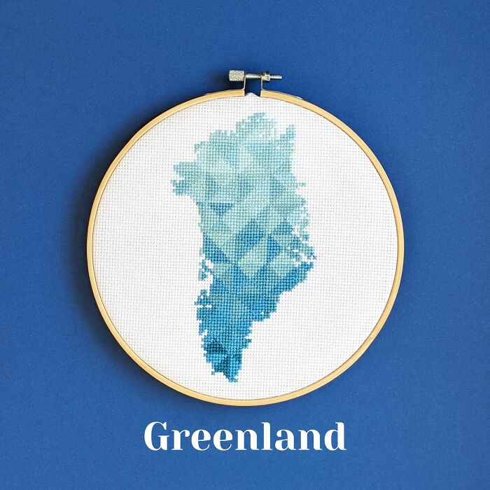 Cross-stitched map of Greenland in blue shades displayed in an embroidery hoop on a blue background.