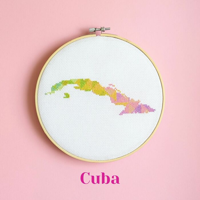 Cross-stitched map of Cuba in multiple colors displayed in embroidery hoop on pink background.