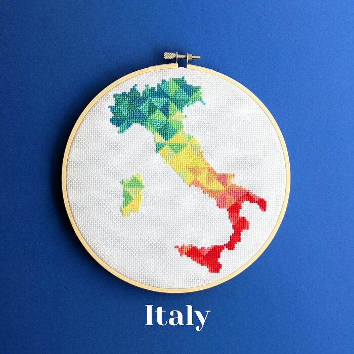 Cross-stitched map of Italy in a rainbow gradient displayed in an embroidery hoop on a blue background.