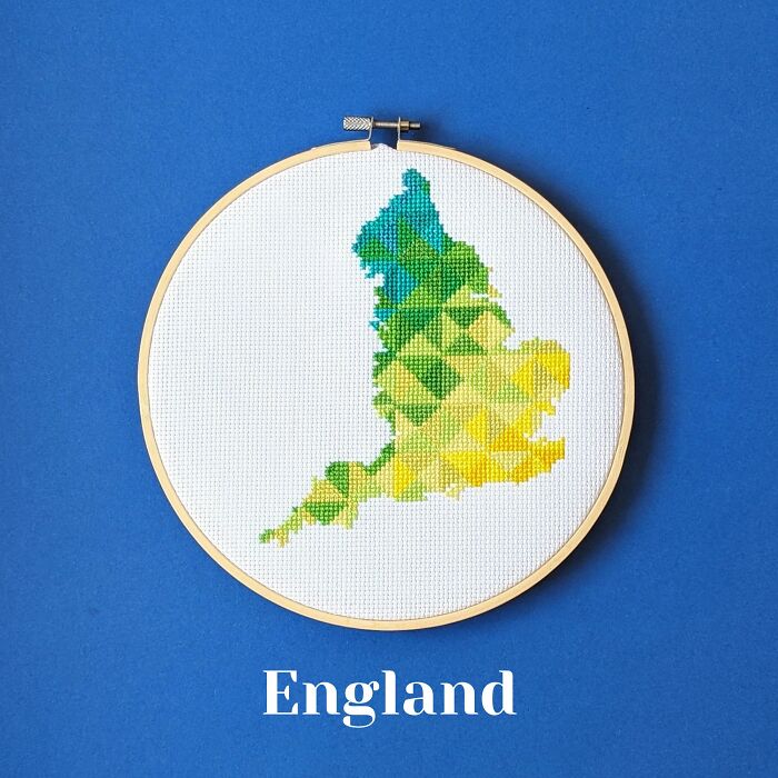 Cross-stitched map of England in green, blue, and yellow threads displayed in an embroidery hoop on a blue background.