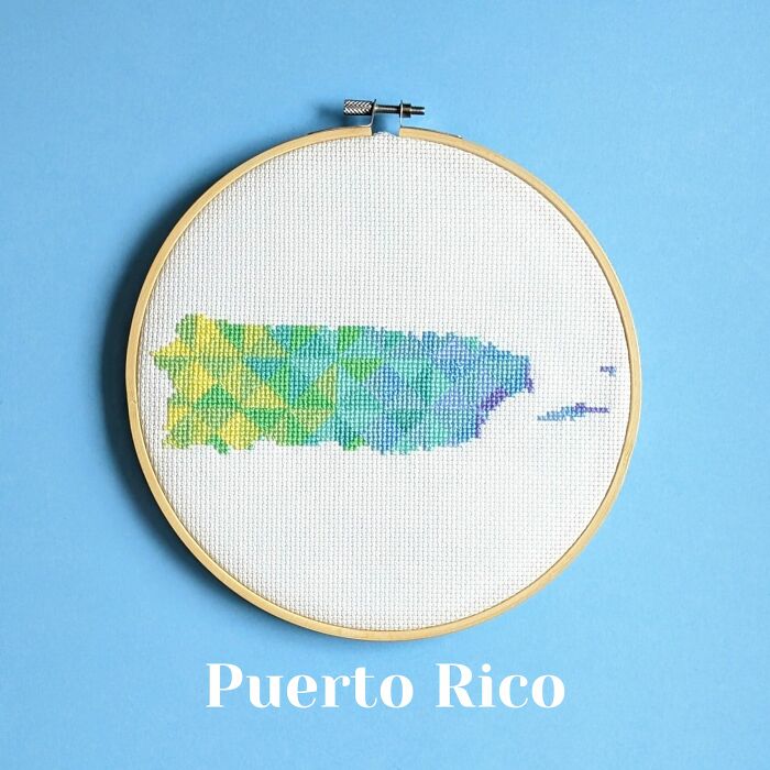 Cross-stitched map of Puerto Rico with colorful geometric patterns in a wooden embroidery hoop on a blue background