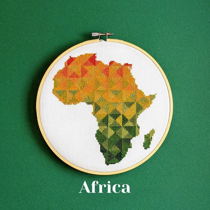 Cross-stitched map of Africa in warm gradient colors embroidered on white fabric in a wooden hoop.